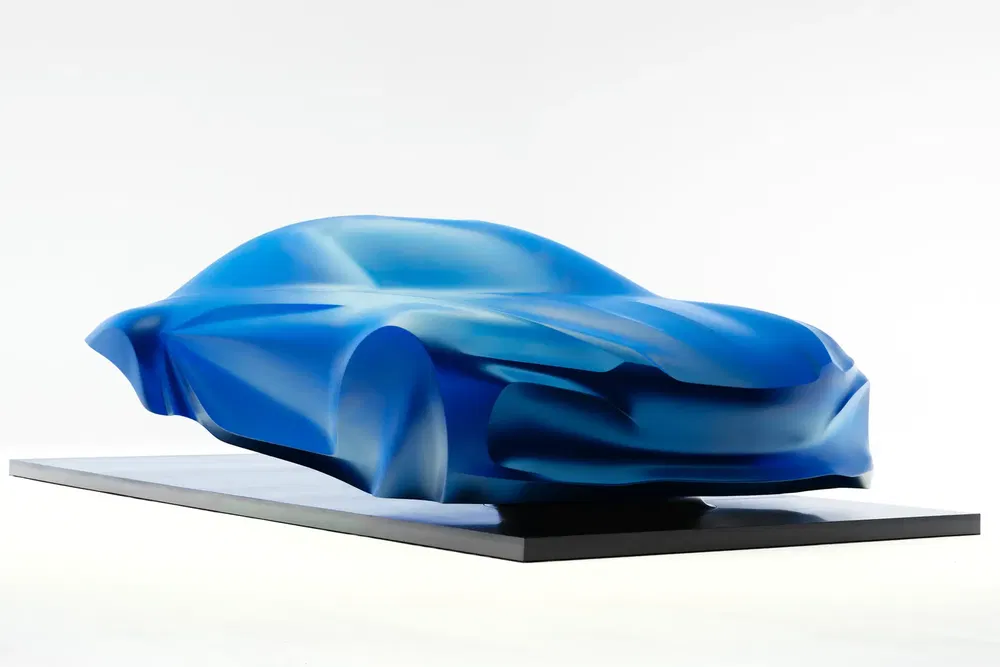 Sculpture abstraite de concept-car bleu aux lignes fluides sur socle noir.