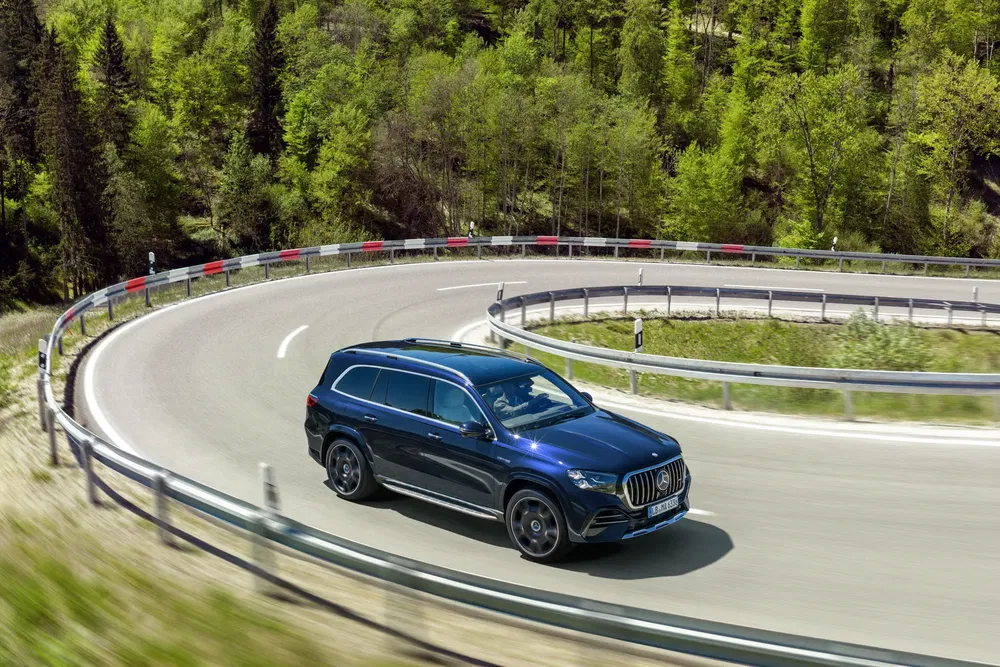 Mercedes-Benz GLS bleu sur une route sinueuse, entourée d'une forêt luxuriante.