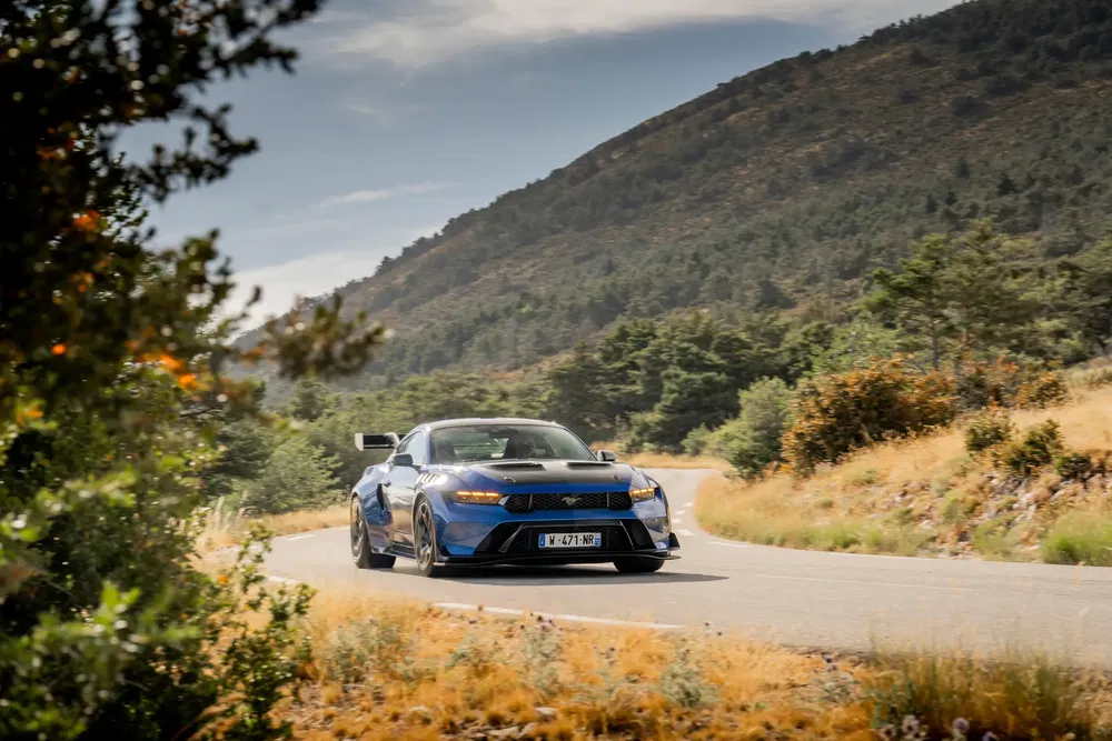 Ford Mustang bleu roulant sur une route de montagne sinueuse par temps clair.