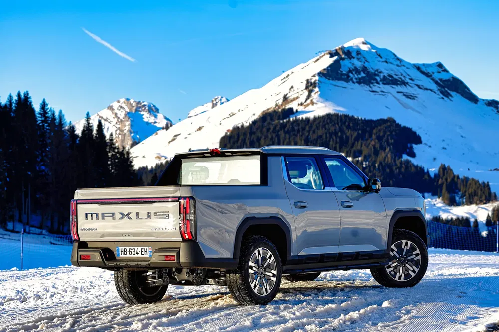 Maxus T90 gris sur neige, montagnes enneigées en arrière-plan, ciel bleu.