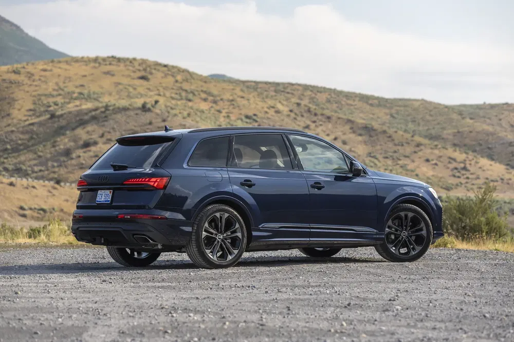 Audi Q7 bleu stationné sur un terrain de gravier avec collines en arrière-plan.