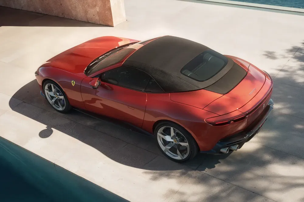 Rode Ferrari Roma Spider op zonnig terras, zwarte softtop en kenmerkende velgen.