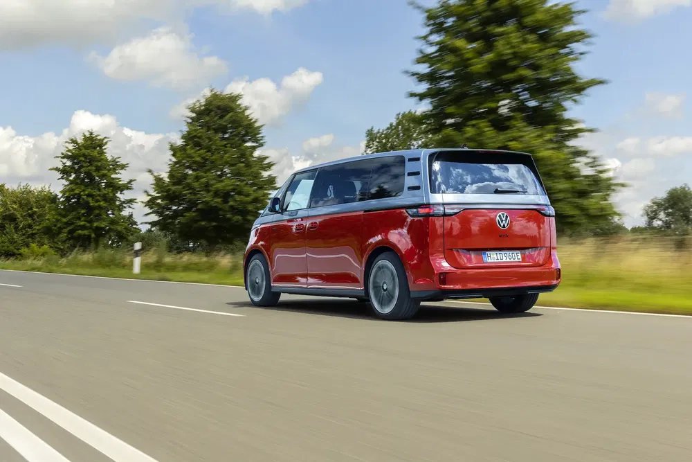 Volkswagen ID.Buzz rouge roulant sur une route dégagée sous un ciel bleu.