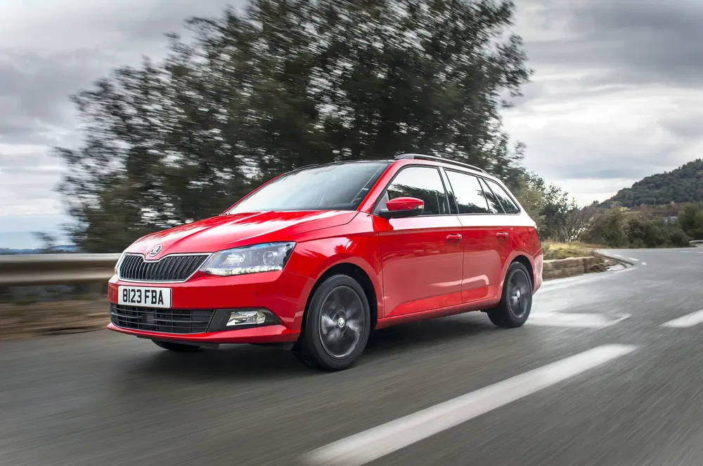 Rode Skoda Fabia rijdt op een kronkelige weg met bosrijke achtergrond.