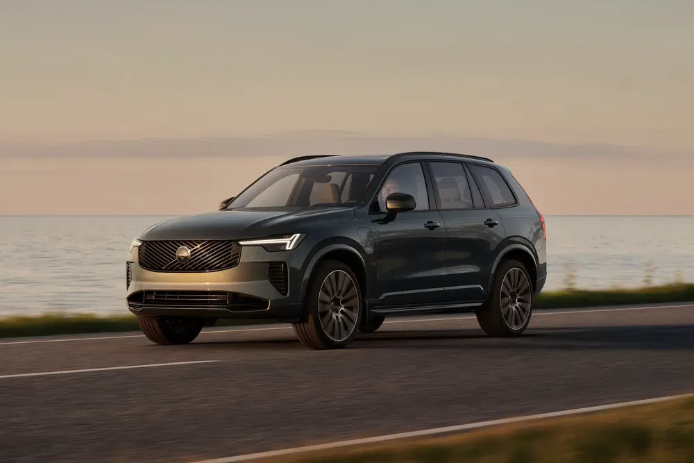 Volvo SUV roulant sur une route côtière au coucher du soleil.