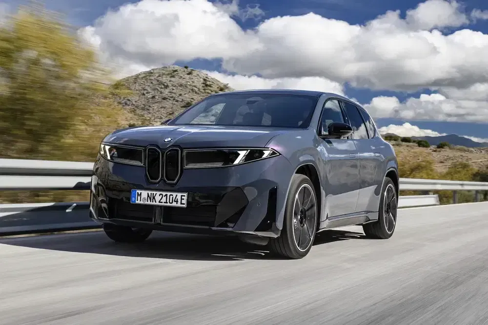 BMW iX roulant sur une route panoramique sous un ciel partiellement nuageux.