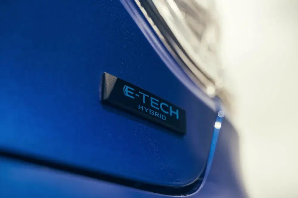 Gros plan sur l'insigne E-Tech Hybrid sur une voiture bleue, symbole d'innovation hybride.