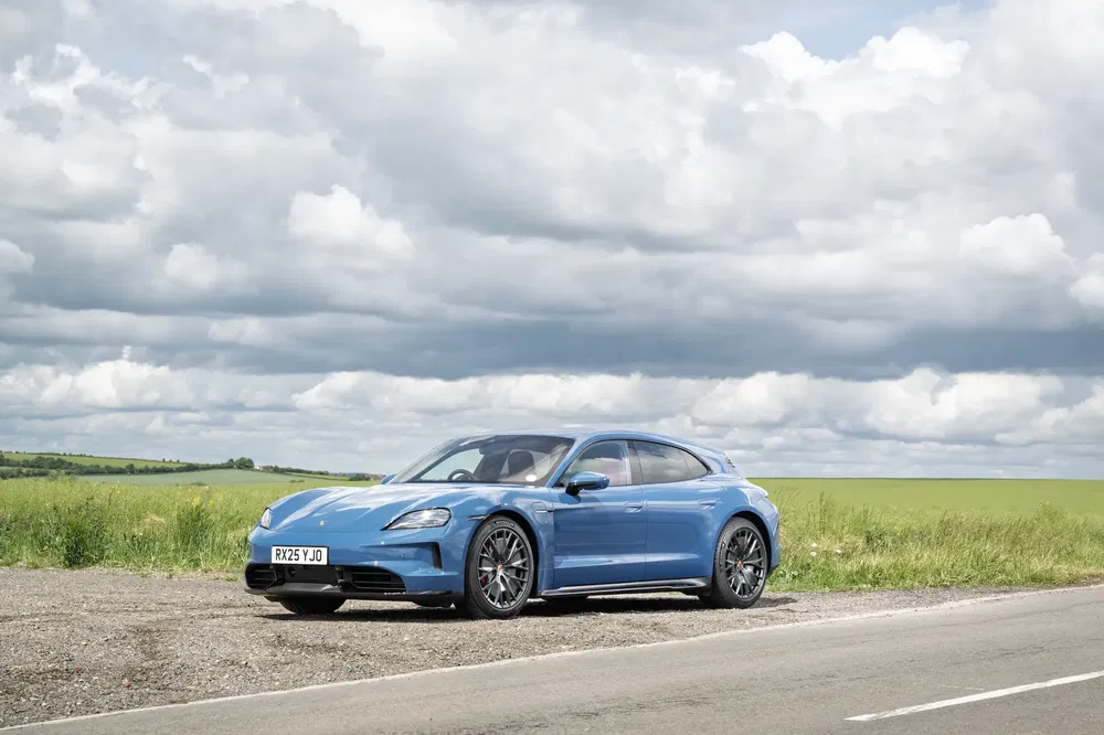 Porsche Taycan Cross Turismo bleue garée sur route de campagne sous un ciel nuageux.