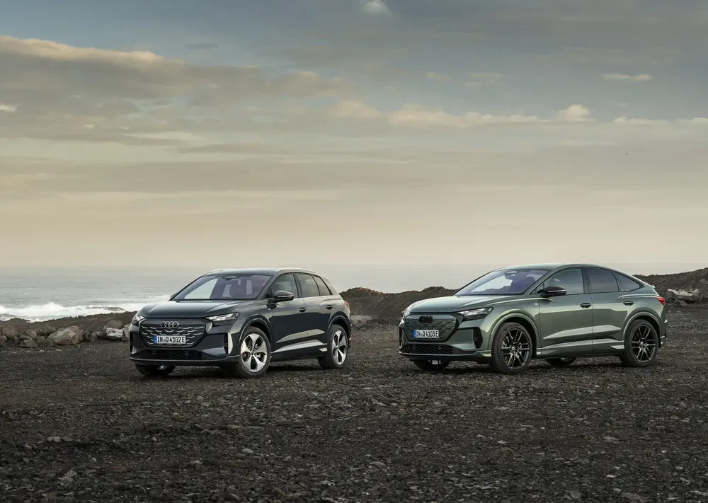 Deux Audi Q4 e-tron électriques garées sur un rivage rocheux avec un ciel nuageux.