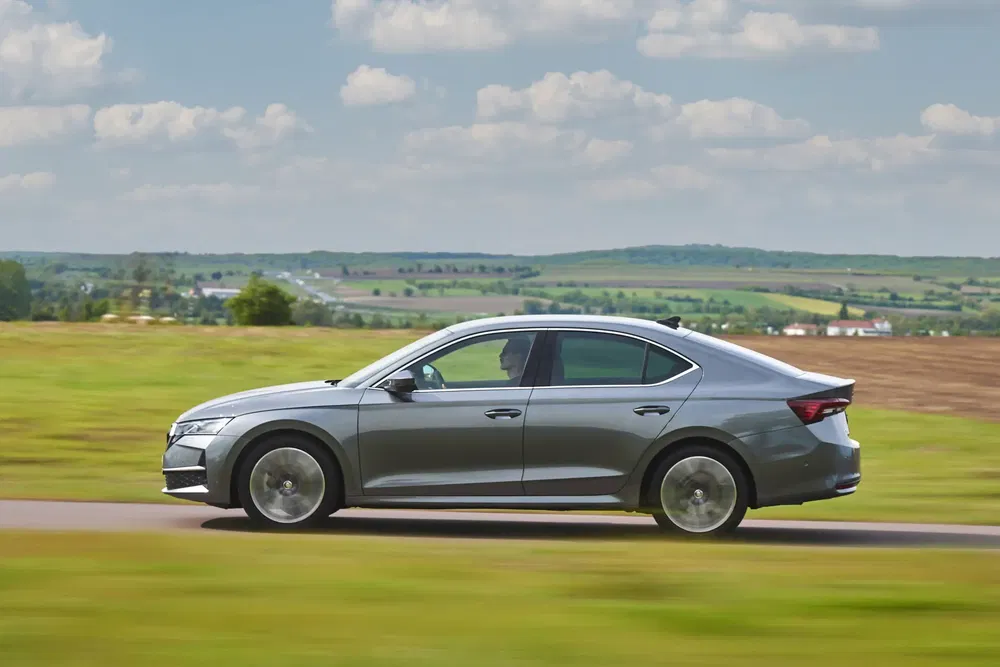 Berline Skoda grise roulant sur route de campagne, paysages verdoyants en arrière-plan.