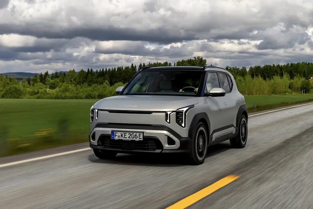 Kia EV5 grise roulant sur une route, ciel nuageux en arrière-plan.