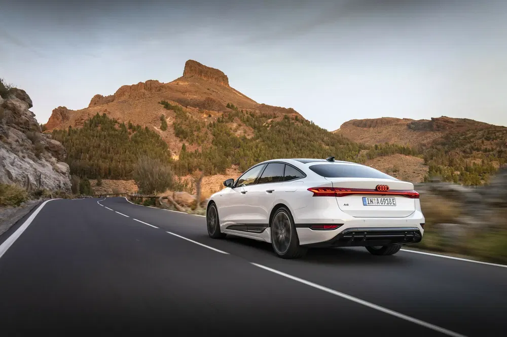Audi A6 blanc sur route de montagne sinueuse au coucher du soleil.