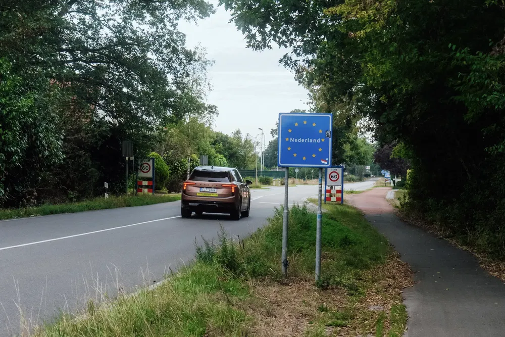 Voiture passant frontière vers les Pays-Bas avec panneau routier européen visible.