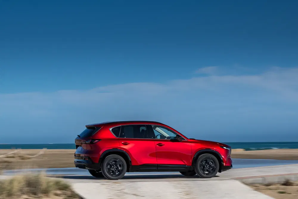 Rode Mazda CX-5 rijdt langs een kustweg met uitzicht op de oceaan.