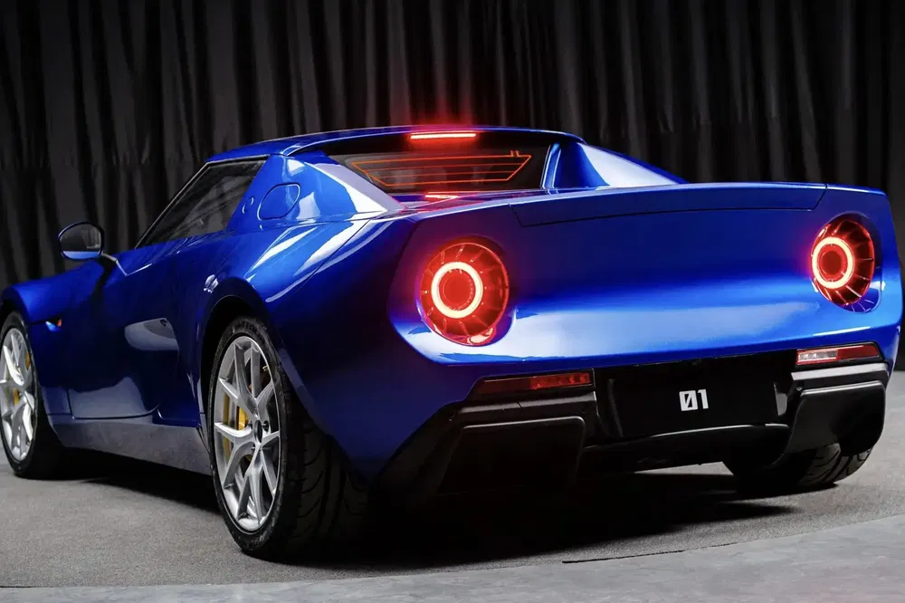 Voiture de sport bleue avec design rétro, éclairage arrière distinctif dans un garage sombre.