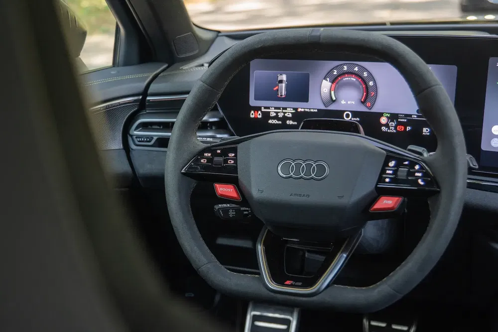 Audi-stuurwiel met modern digitaal dashboard op de achtergrond.