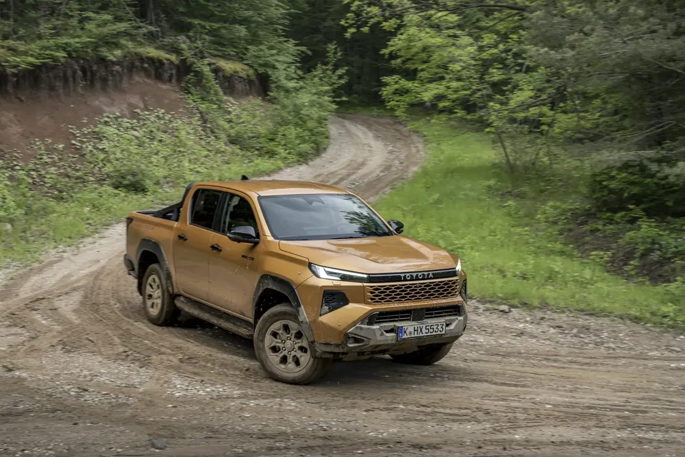 Toyota pickup marron sur un chemin de terre sinueux en forêt dense.