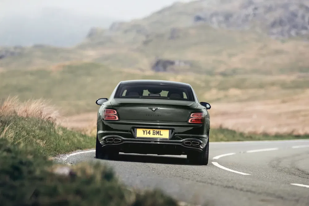 Bentley Flying Spur verte sur une route de campagne sinueuse, paysage montagneux en arrière-plan.