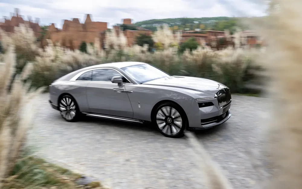 Rolls-Royce Spectre grise roulant sur une route bordée de végétation luxuriante.