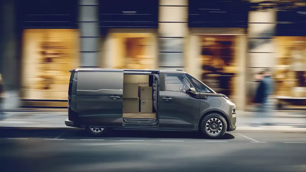 Fourgon électrique Rivian EDV roulant avec portes ouvertes, montrant des cartons à l'intérieur.