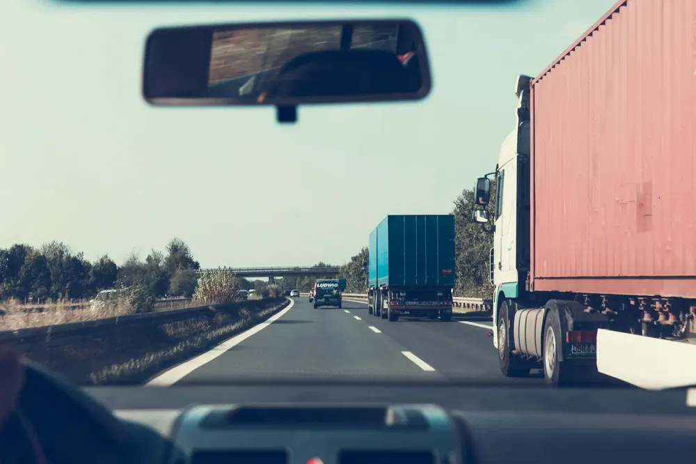 {"fr":"Vue intérieure d'une voiture dépassant des camions sur une autoroute bordée d'arbres.","nl":"Binnenaanzicht van een auto die vrachtwagens inhaalt op een met bomen omzoomde snelweg."}