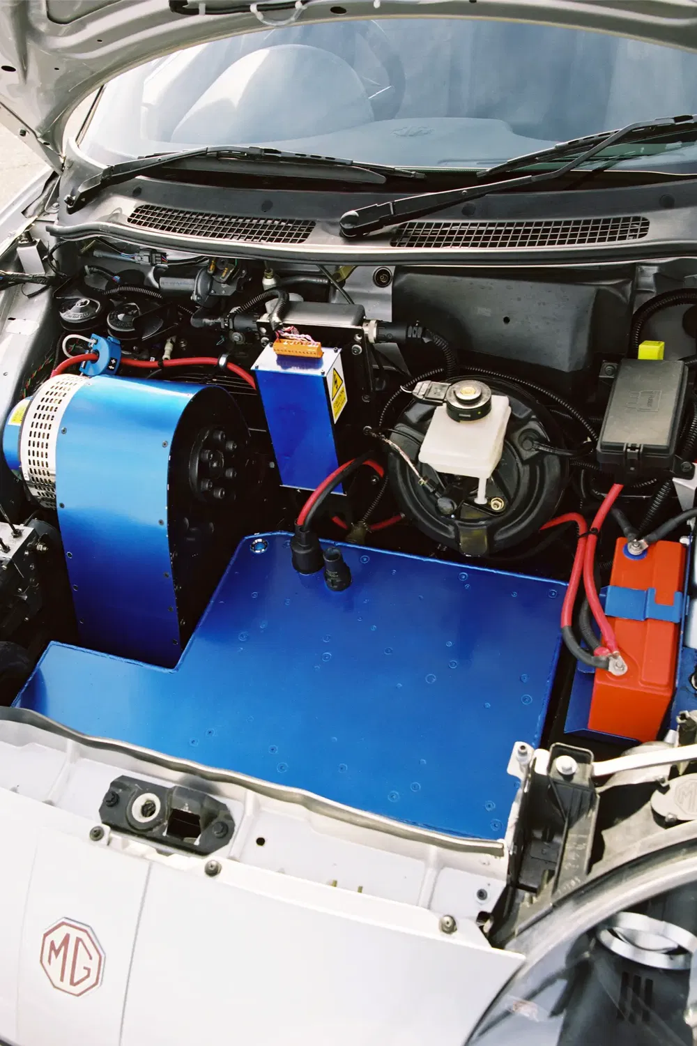 Compartiment moteur d'une voiture MG avec conversion électrique et câblage visible.