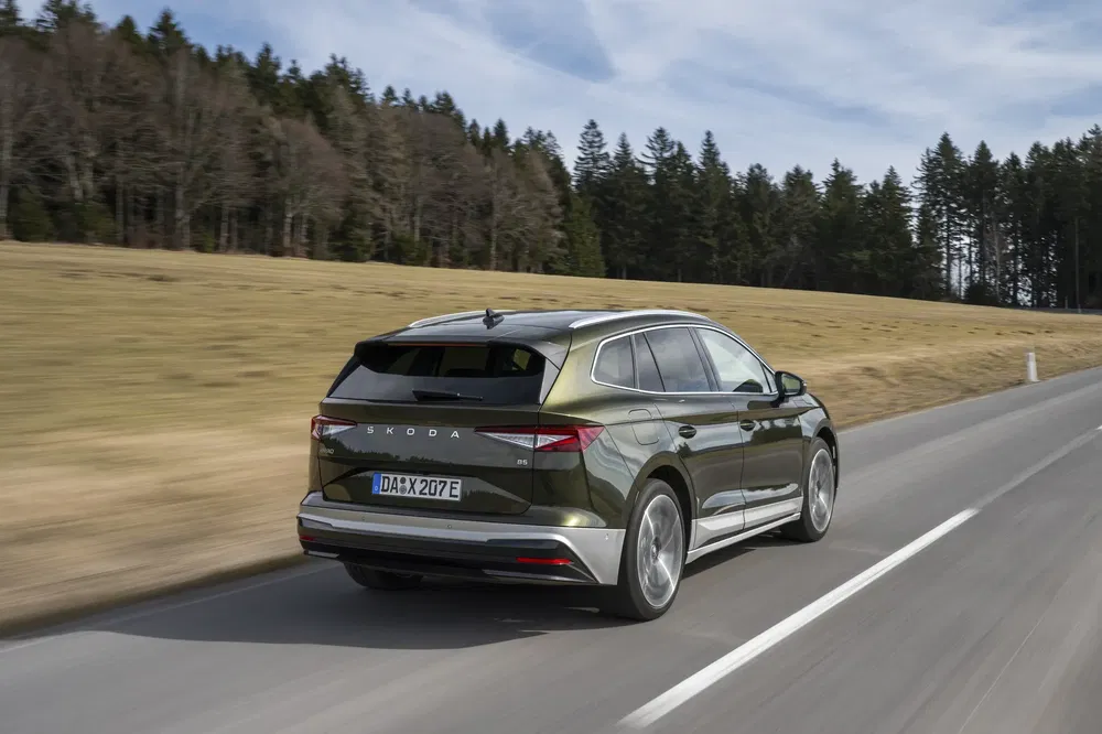 La Skoda Enyaq iV verte roule sur une route de campagne bordée d'arbres.