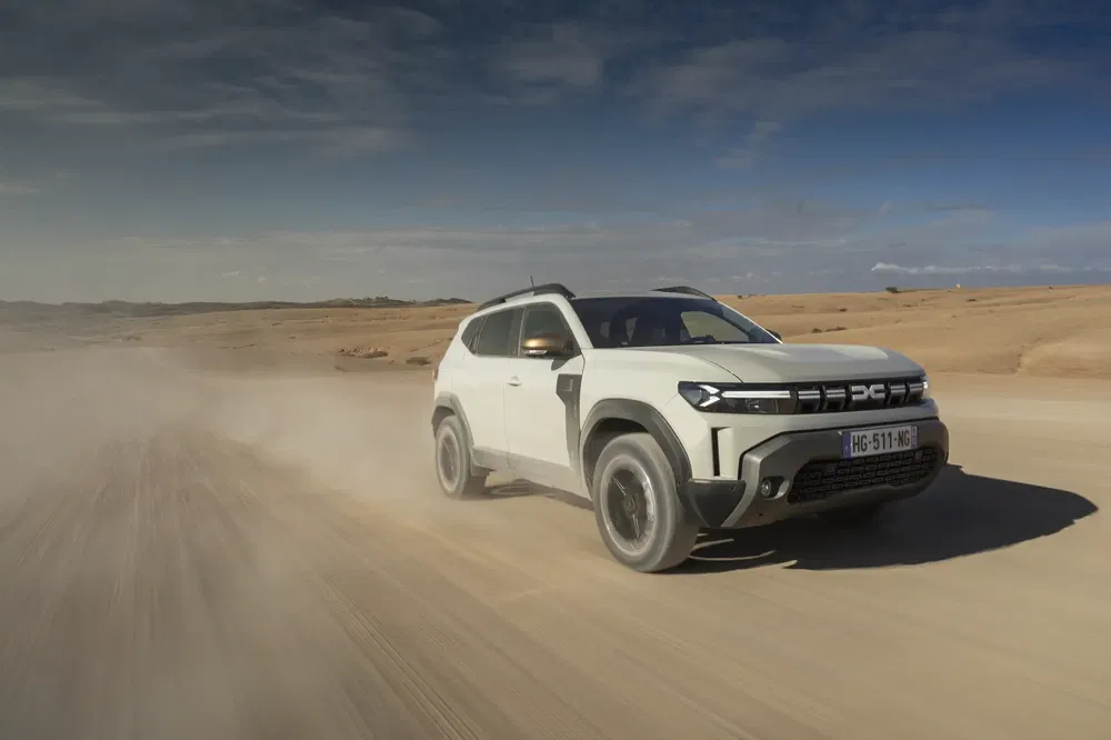Witte Dacia Duster SUV rijdt op zanderige weg in een woestijn onder heldere hemel.