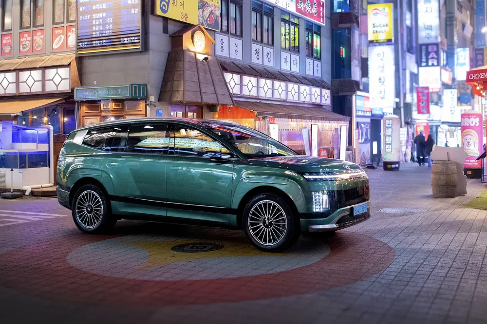 SUV vert stationné en ville asiatique animée avec panneaux lumineux colorés de nuit.