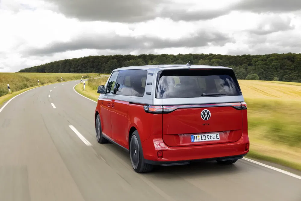 Volkswagen ID. Buzz rouge sur route de campagne sinueuse en arrière-plan sombre.