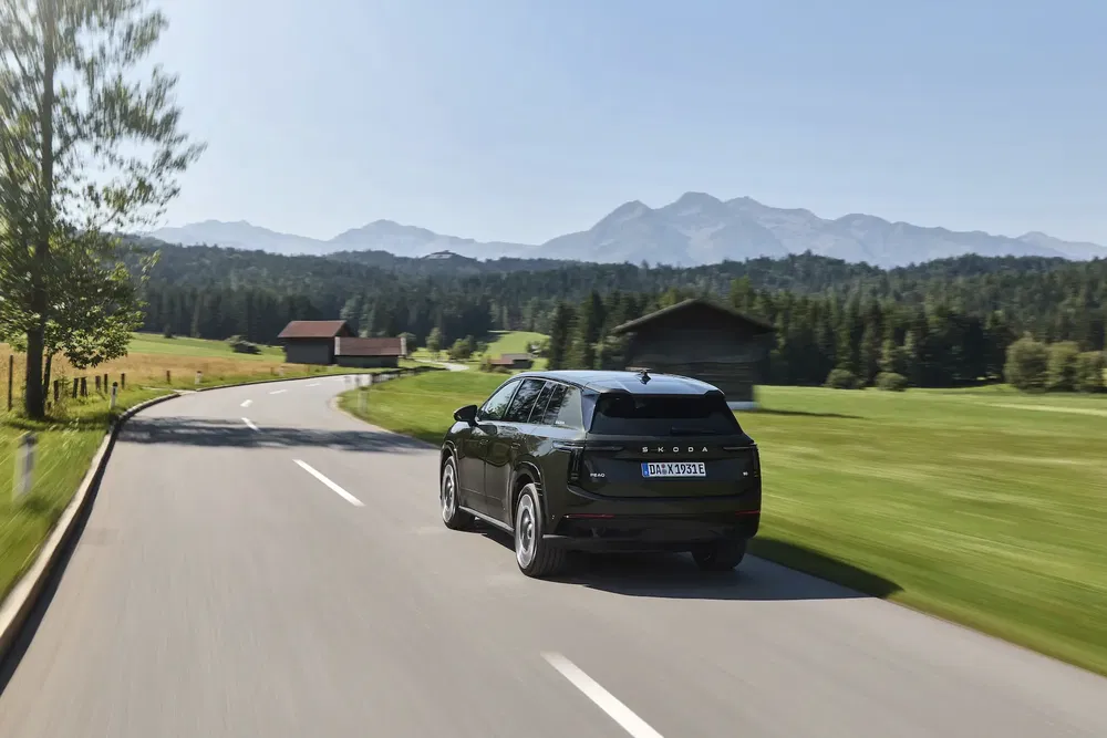 Zwarte Skoda SUV rijdt op landweg met bergen op de achtergrond.