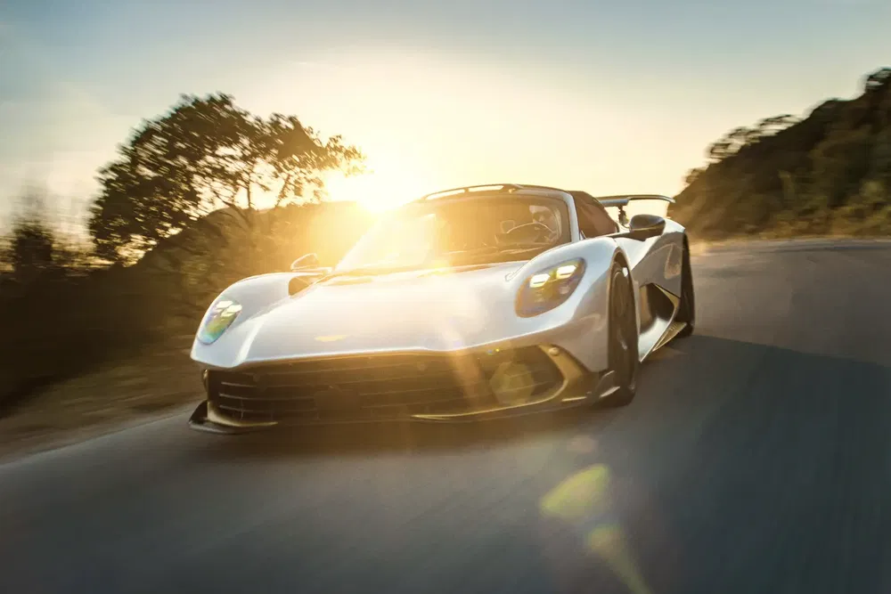 {"fr":"Aston Martin Valhalla roulant au crépuscule sur une route sinueuse, soleil en arrière-plan.","nl":"Aston Martin Valhalla rijdt bij zonsondergang op een kronkelende weg met zonlicht op de achtergrond."}