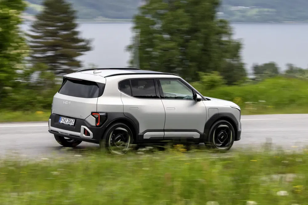 SUV Kia EV9 argenté roulant sur route de campagne avec arrière-plan verdoyant.