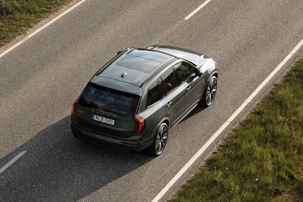 Volvo XC90 vert roulant sur une route de campagne ensoleillée.