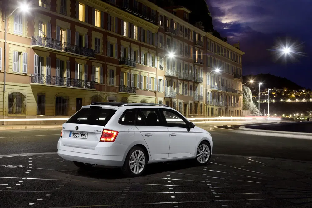 Witte Skoda Fabia geparkeerd voor verlichte gebouwen 's nachts.
