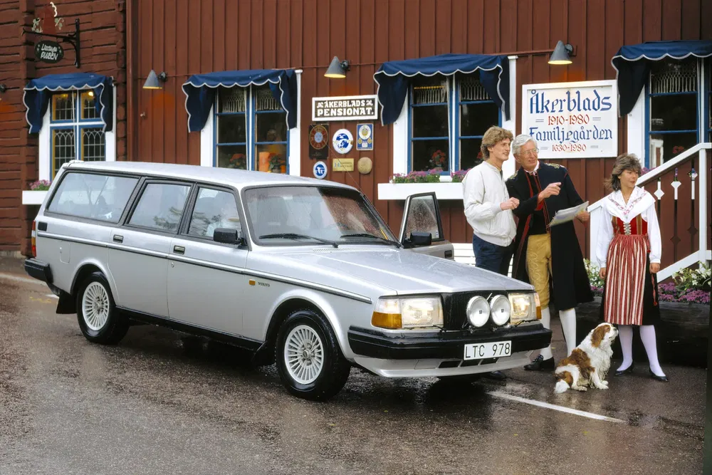 Voiture Volvo argentée garée devant une pension suédoise traditionnelle avec des personnes en costumes.