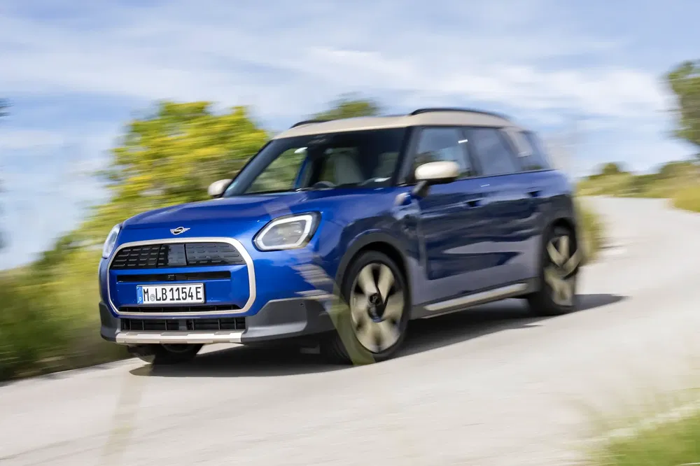 Blauwe Mini Countryman rijdt op bochtige weg bij zonnig weer.