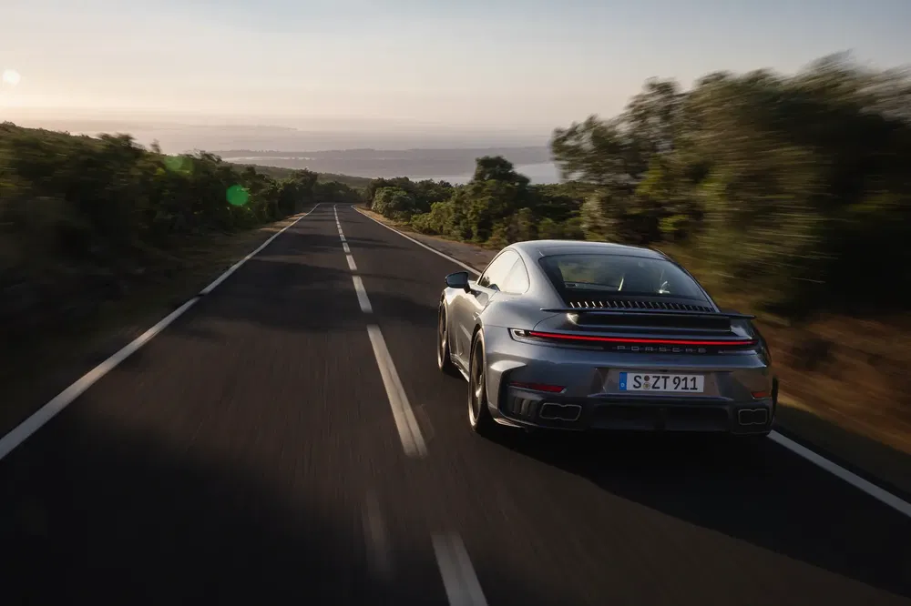 Porsche 911 argentée sur route panoramique au coucher du soleil.