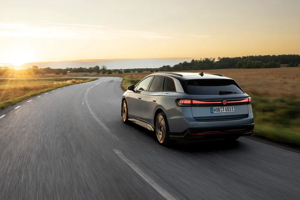 Volkswagen ID.7 break roulant sur route bordée de champs au coucher du soleil.