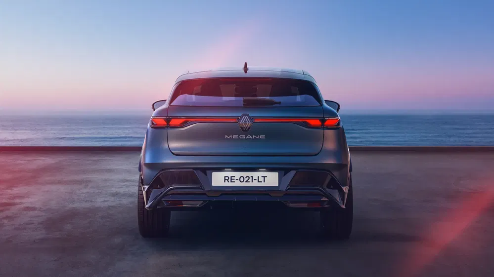 Achteraanzicht van een elektrische Renault Mégane met zee op de achtergrond bij zonsondergang.