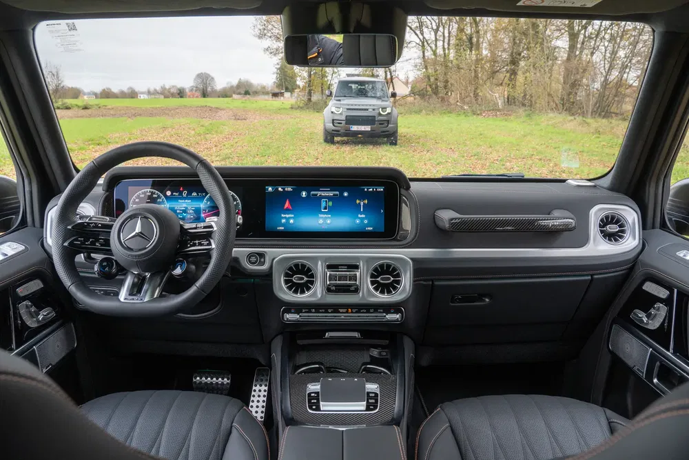 Intérieur de Mercedes-Benz G-Class avec écran d'affichage numérique, vue vers un Land Rover Defender.