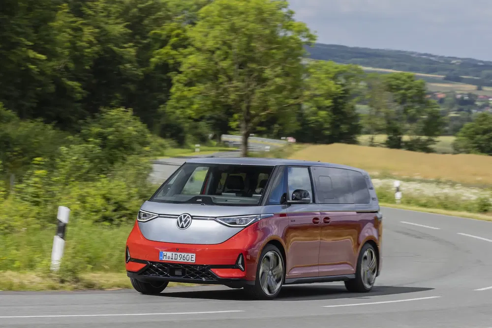 Volkswagen ID. Buzz électrique rouge sur route de campagne ensoleillée.