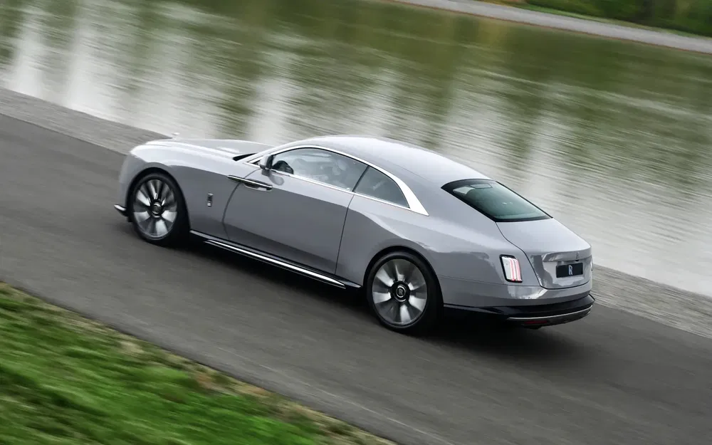 Rolls-Royce Spectre argent moderne roulant près d'un lac, design élégant et luxueux.