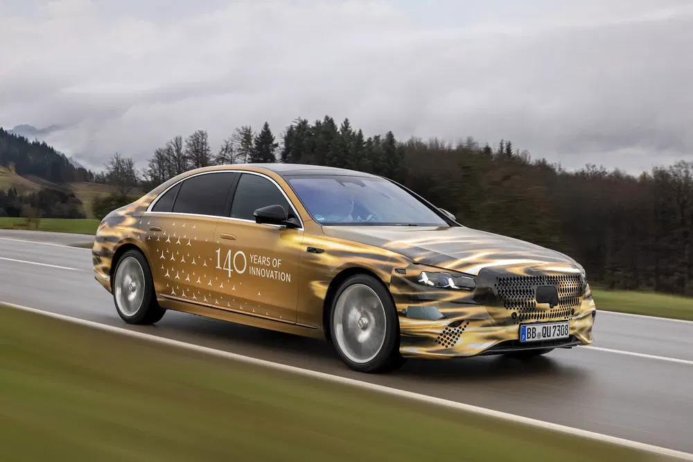 {"fr":"Voiture Mercedes-Benz dorée sur route de campagne, célébrant 140 ans d'innovation.","nl":"Gouden Mercedes-Benz auto op plattelandsweg, viert 140 jaar innovatie."}