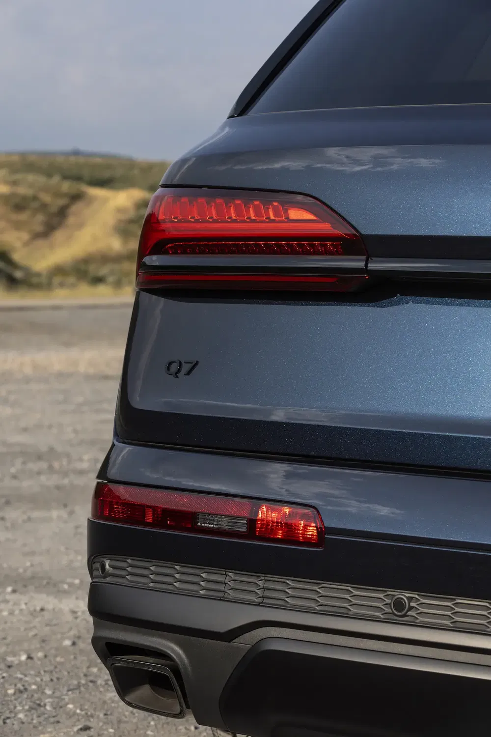 Feux arrière et logo Audi Q7 sur un SUV gris moderne sur fond de campagne.