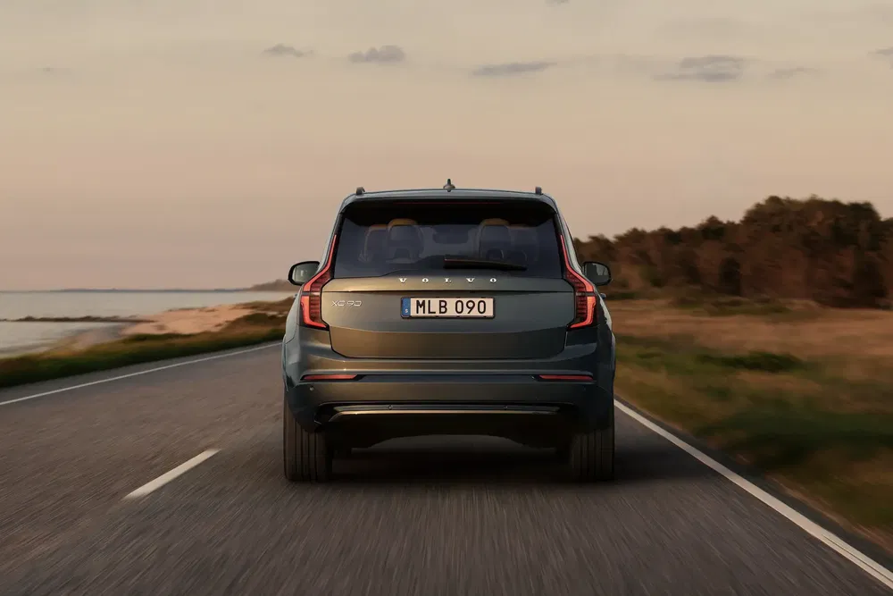Volvo XC90 roulant sur une route côtière au coucher du soleil.