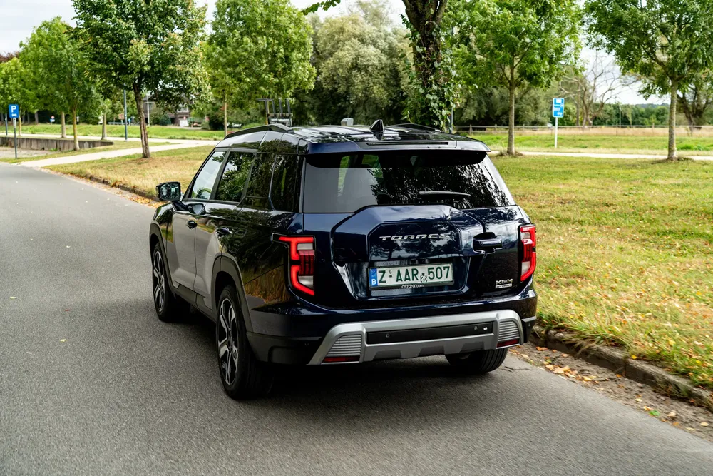 SUV SsangYong Torres noir roulant sur une route bordée d'arbres en pleine journée.