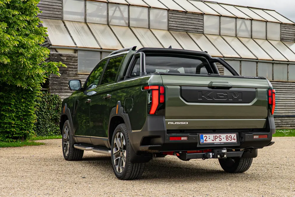 Pick-up Ssangyong Musso vert devant hangar en verre, vue arrière avec plaque belge.