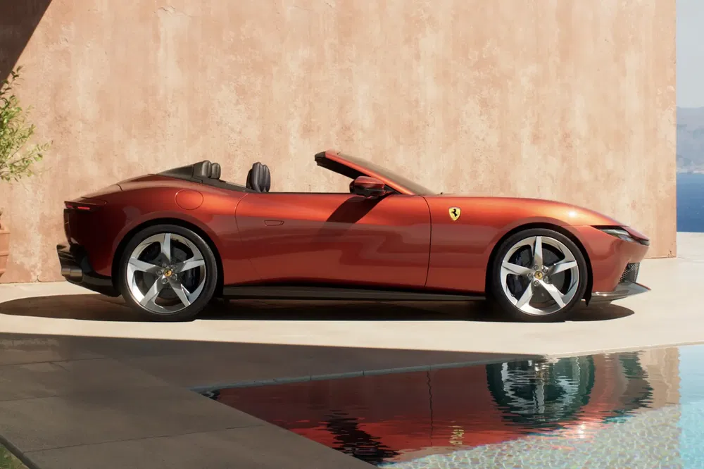 Rode Ferrari Roma Spider geparkeerd naast een zwembad met een beige muur op de achtergrond.