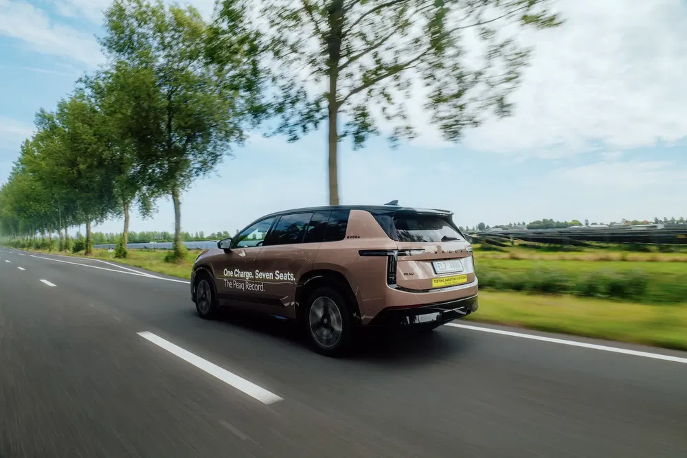 SUV électrique marron sur route bordée d'arbres, mettant en avant l'autonomie d'une charge.